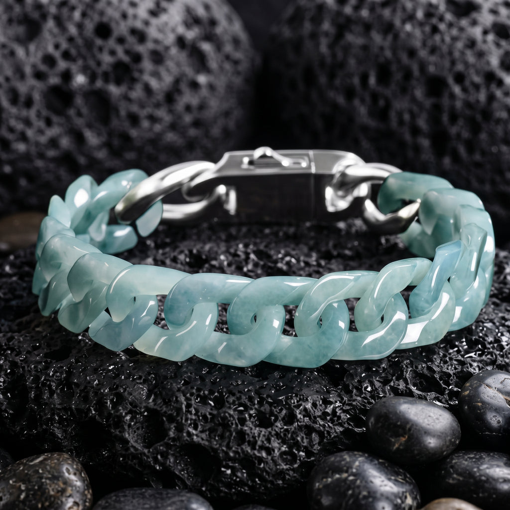 A blue Jade cuban-link bracelet with light blue-green jade-like links, displayed on dark volcanic rocks and smooth black stones.