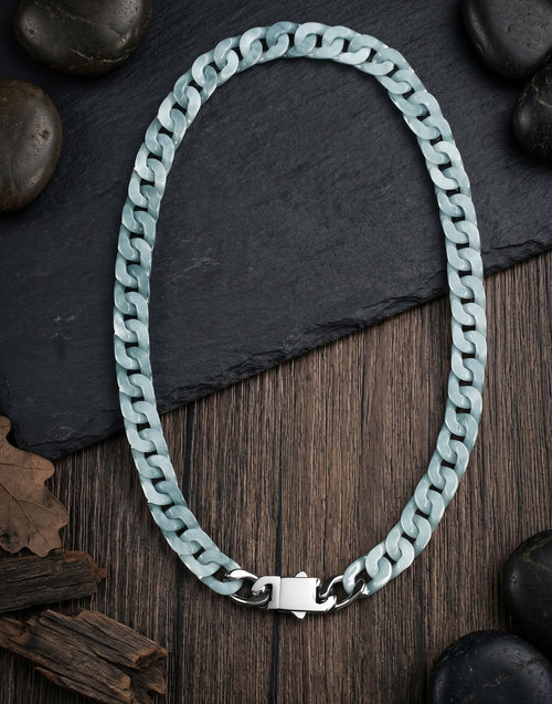 A chunky cuban-link jade chain necklace in a pale icy blue-green hue with a polished silver clasp, displayed on a dark slate and rustic wood background with decorative stones.