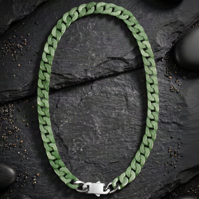 A green cuban-link chain necklace with a silver clasp, arranged in an oval shape on a dark textured slate background.