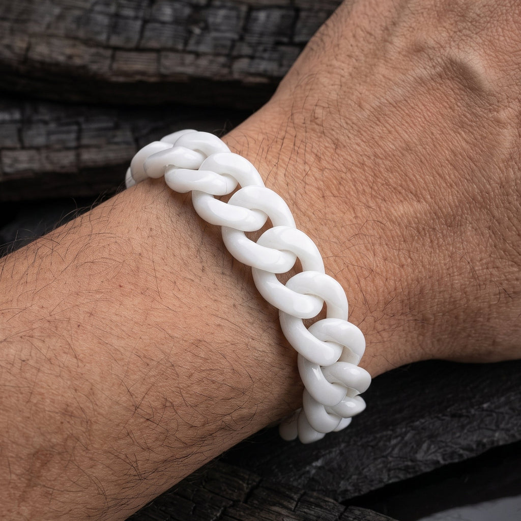 A white jade cuban chain bracelet worn on a person's wrist, shown in a close-up shot against a dark textured wood background.
